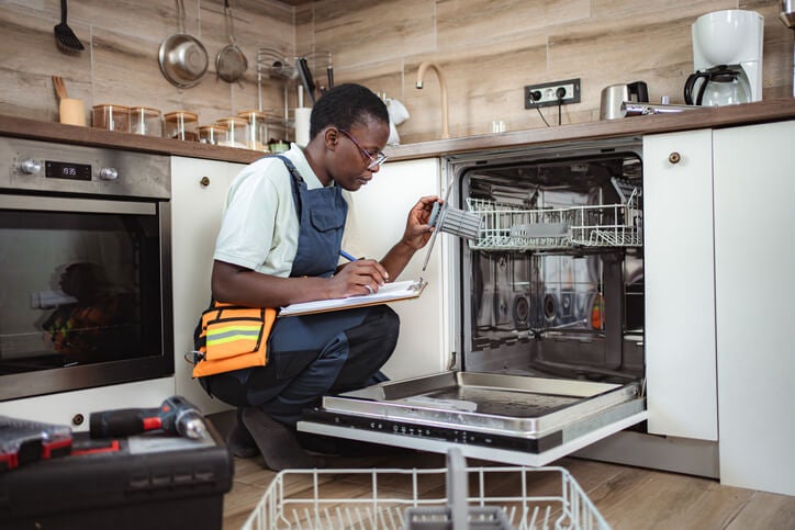 A man in an apron repairs a dishwasher, showcasing appliance maintenance in Keller, TX