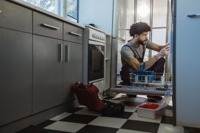 A man repairs a dishwasher in a kitchen, highlighting appliance maintenance in Keller, TX