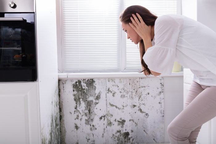 A woman stands before a moldy wall, highlighting risks of water and mold damage in Keller, TX