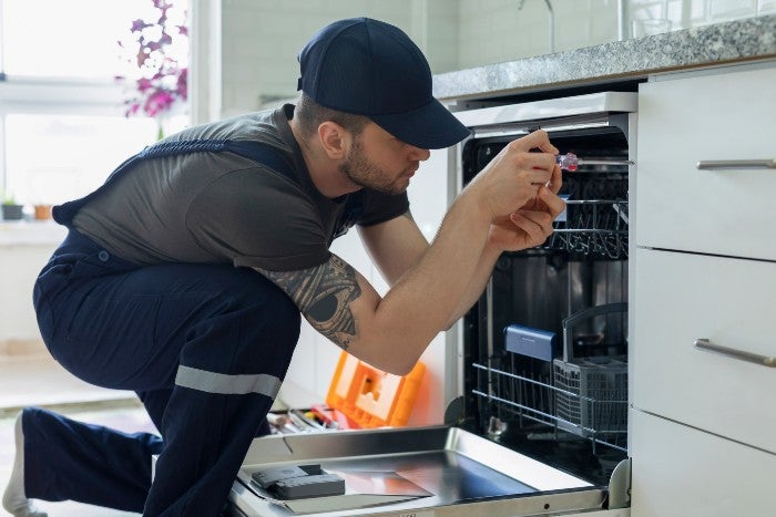 Professional technician repairing dishwasher in kitchen appliance repair service in Keller, TX